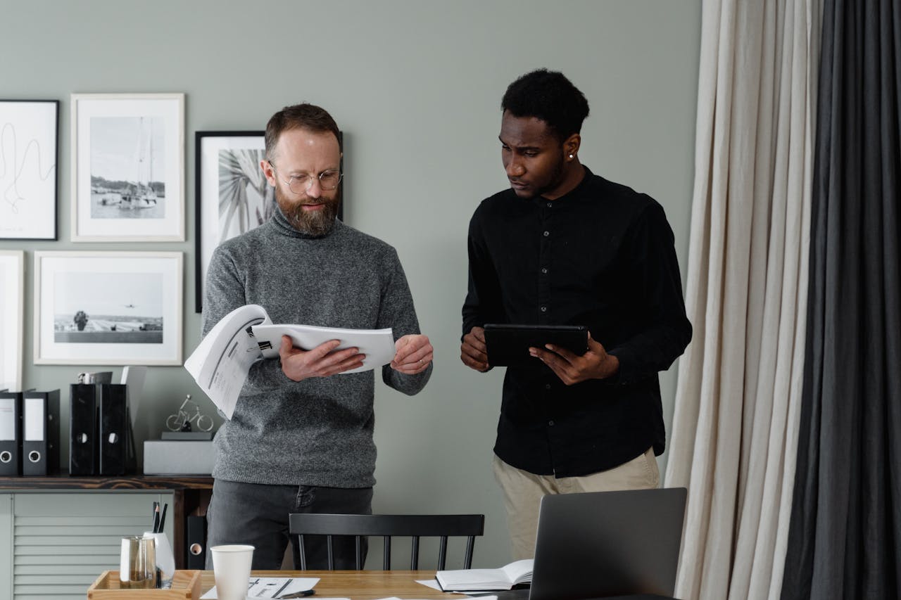 Two professionals reviewing documents and using a tablet in a modern office setting.