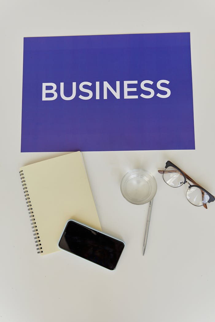 A business-themed flat lay with essentials like a notebook, smartphone, glasses, and a sign.